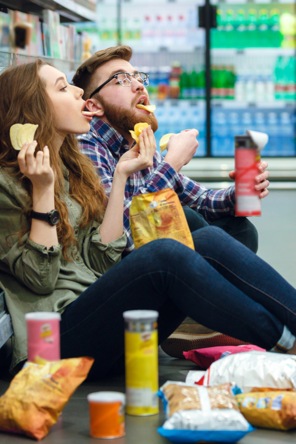 couple eating chips in the middle of the grocery store aisle